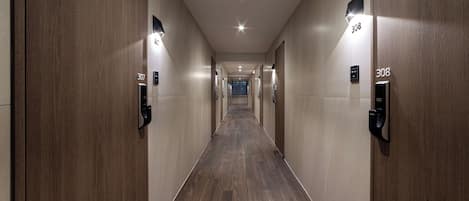 A long, narrow hallway with wooden paneling and numbered doors, leading to a distant exit.
