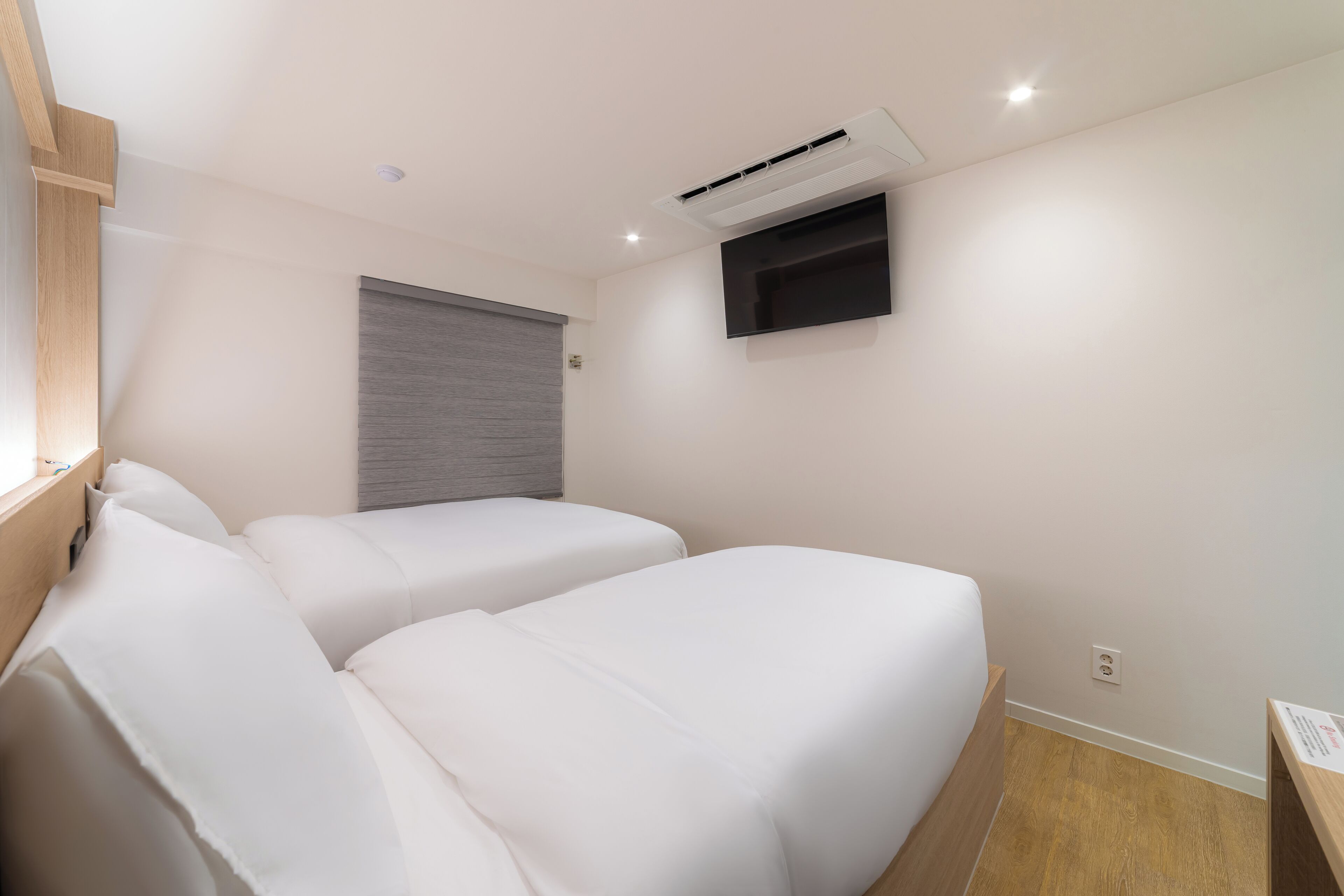 Una habitación de hotel moderna con dos camas, un televisor de pantalla plana en la pared y un ventanal con persiana bajada.