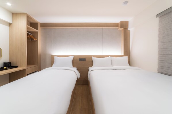 Una habitación de hotel moderna con dos camas individuales, un armario de madera y una mesita de noche.