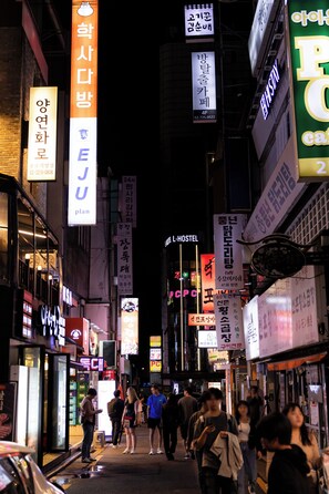Una concurrida calle urbana de noche, con varios letreros comerciales y algunos peatones.