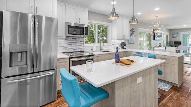 Una cocina moderna con electrodomésticos de acero inoxidable, una isla central y taburetes azules.