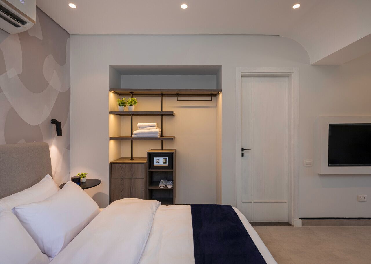 Habitació d'hotel moderna amb un llit gran, un televisor fixat a la paret i un armari de paret amb prestatges.