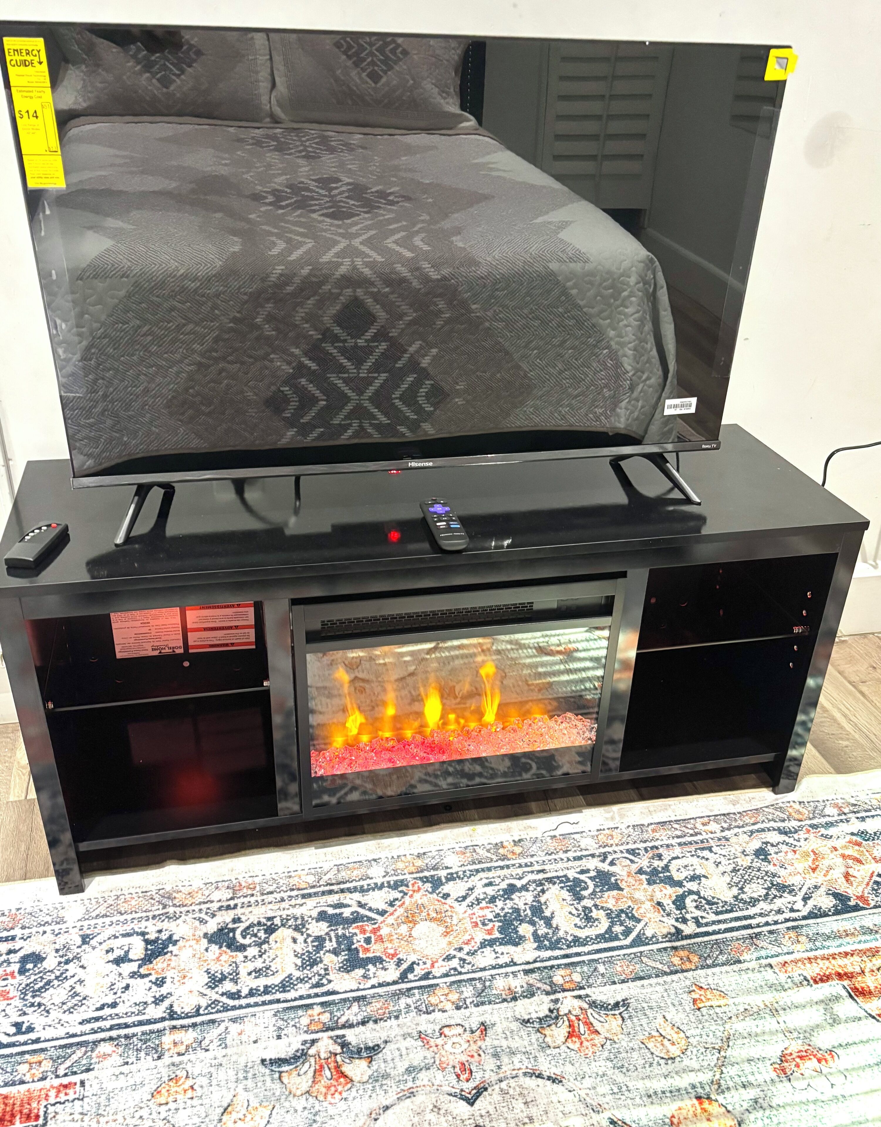 A Hisense TV on a black stand with a fireplace below it.