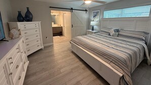 Ein Schlafzimmer mit Bett, Schminktisch, Kommode, Deckenventilator und Blick ins Badezimmer.