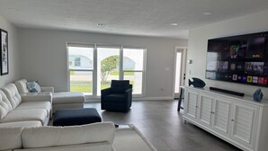 Ein geräumiges Wohnzimmer mit großem Flachbildfernseher, einer Couch, einem Sessel und einem Schrank.
