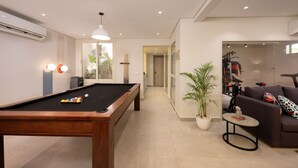 Ein modernes Wohnzimmer mit Billardtisch, einer Couch, einem kleinen Tisch und Trainingsgeräten.