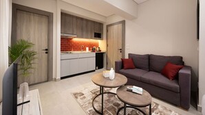 Un ambiente compatto con angolo cottura, un divano grigio, un piccolo tavolino e una TV.