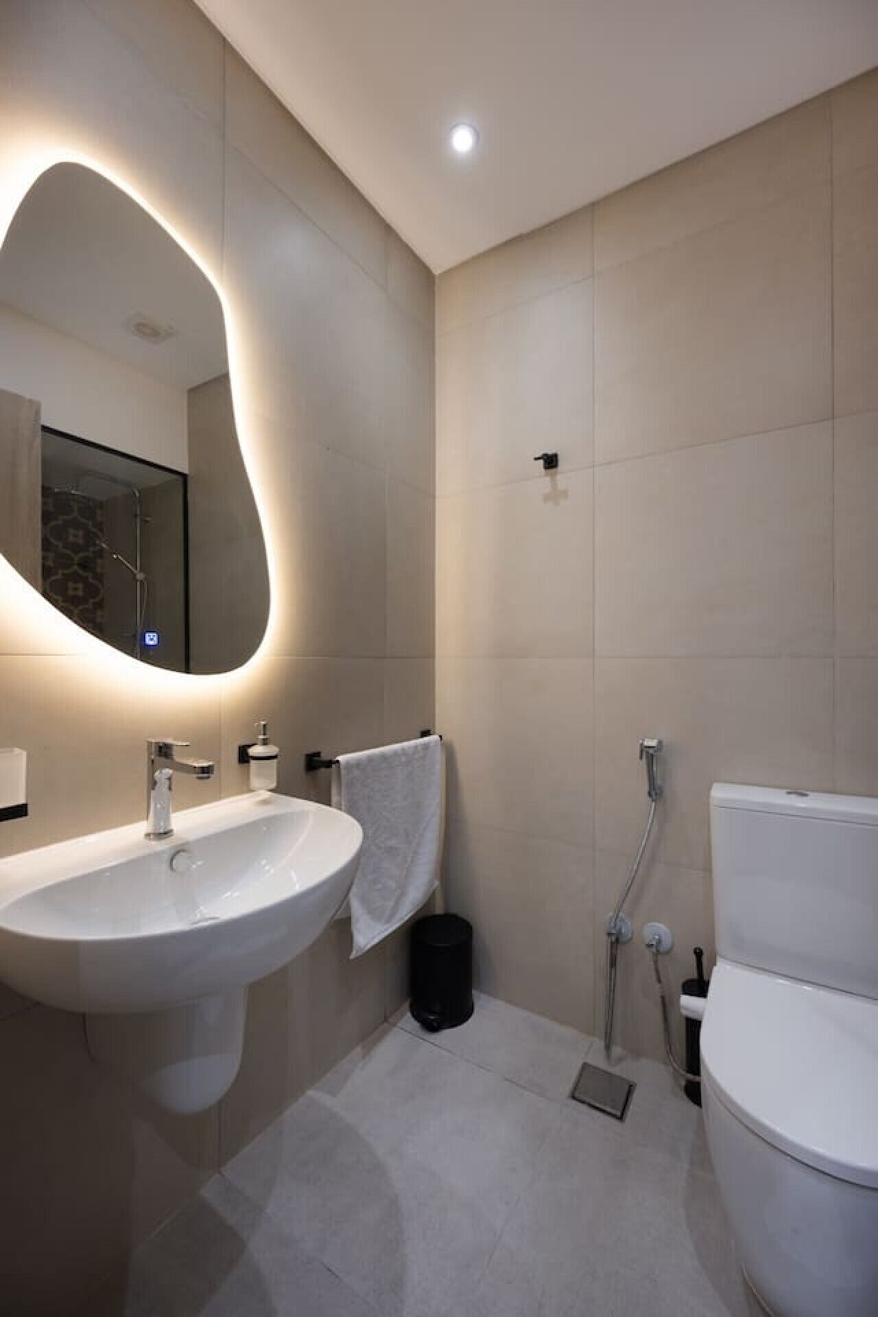 A modern bathroom with a large mirror, a white sink, a toilet, and a shower.