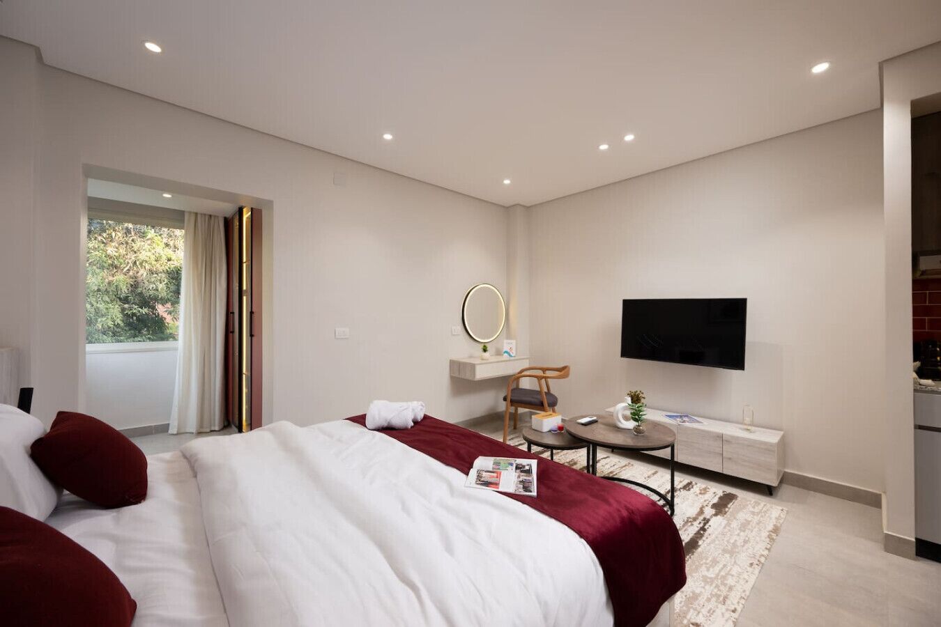 Habitación de hotel moderna con una cama grande, un escritorio, un televisor de pantalla plana y un balcón con cortinas.