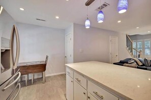 Una cocina moderna con una isla grande, un comedor con mesa de madera y una escalera que sube a un nivel superior.