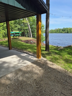 A covered outdoor area with a gravel path leading to a lake, surrounded by trees and a green vehicle.