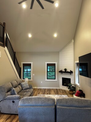 A spacious living room with a gray sectional sofa, a fireplace, and a staircase. - Leaning Oaks Cabin in the woods with waterfront (NEW) (Centreville)