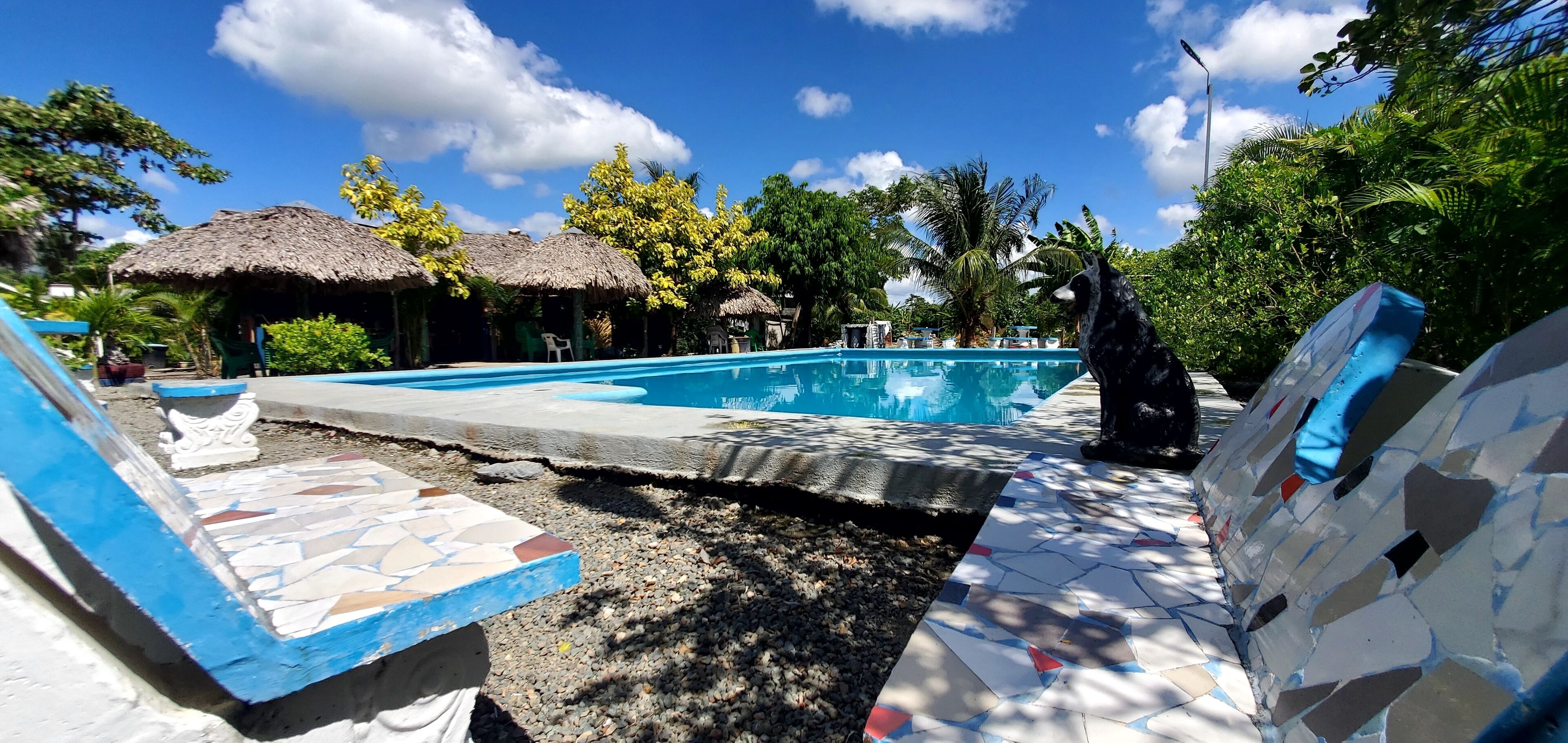 A swimming pool with a tiled deck, surrounded by thatched-roof huts and lush greenery.