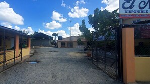Un estacionamiento cerrado con suelo de tierra, un edificio amarillo y un letrero que indica una zona de piscina.