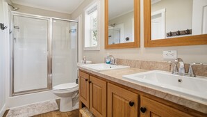 Un bagno moderno con doccia vetro, WC, mobiletti in legno e due lavabi.