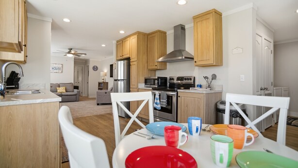 Una cucina moderna con mobili in legno, elettrodomestici in acciaio inossidabile e una zona pranzo con sedie bianche e piatti colorati.