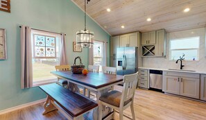 A modern kitchen with wooden cabinets, a stainless steel refrigerator, and a dining area with a bench and chairs. - Pet Friendly, Golf Cart Access, Old Town Location (Port Aransas)