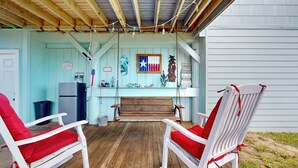 A covered porch with two white chairs with red cushions, a wooden bench, and a hanging light fixture. - Pet Friendly, Golf Cart Access, Old Town Location (Port Aransas)