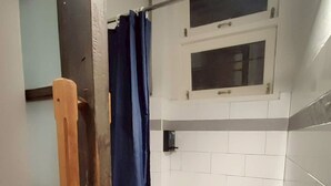 Ein Badezimmer mit weiß gefliesten Wänden, einer Duschvorhang und einem Fenster über dem Waschbecken.