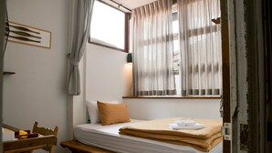 Ein Einzelbett mit Holz Kopfteil, ein Nachttisch, ein Sessel und ein Fenster mit Vorhängen.