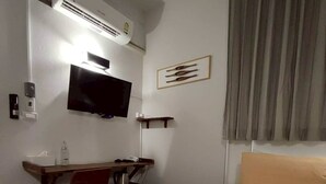 Ein Hotelzimmer mit Bett, Schreibtisch, Fernseher und einer Wandklimaanlage.