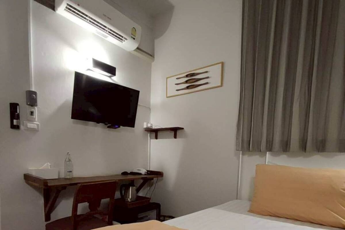 A hotel room with a bed, a desk, a television, and a wall-mounted air conditioner.