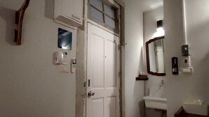 Ein schmaler Flur mit einer weißen Tür, einer kleinen Stufe zum Badezimmer und einem Spiegel an der Wand.