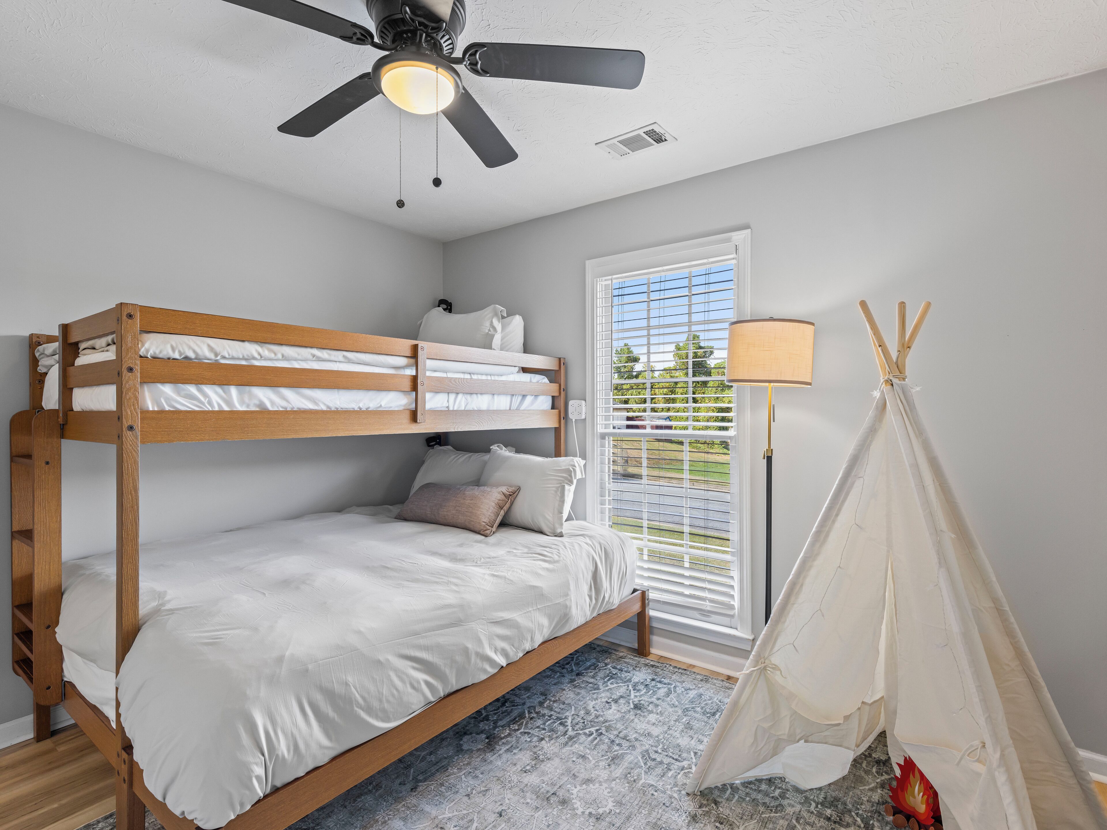 Ein Etagenbett mit Deckenventilator, ein Fenster mit Jalousien und ein Zelt im Teepee-Stil.