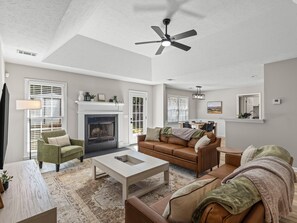 A spacious living room with a fireplace, a ceiling fan, and a dining area with a table and chairs.