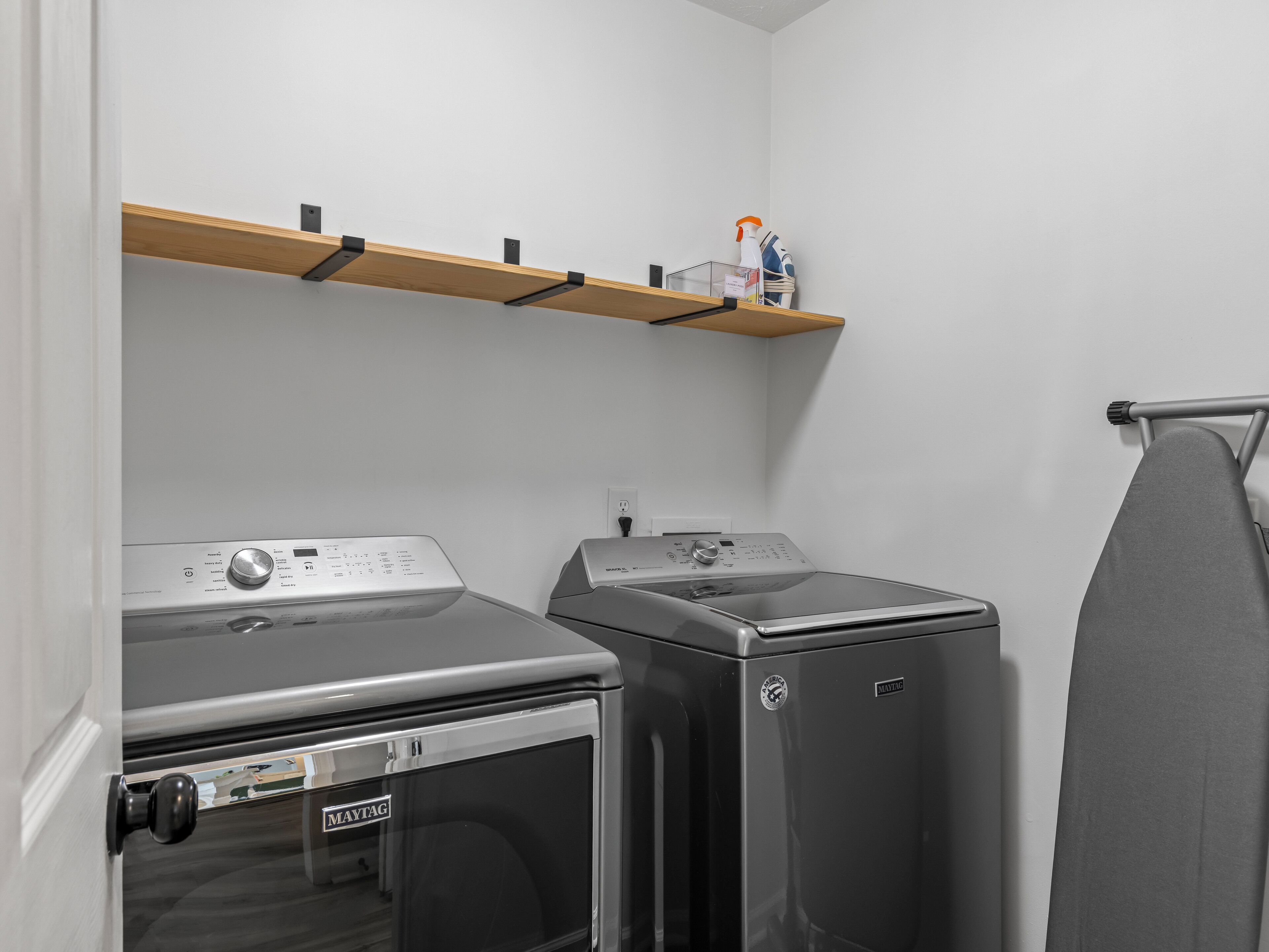 Une buanderie équipée de deux machines à laver, d’un sèche-linge et d’une étagère située au-dessus des machines.