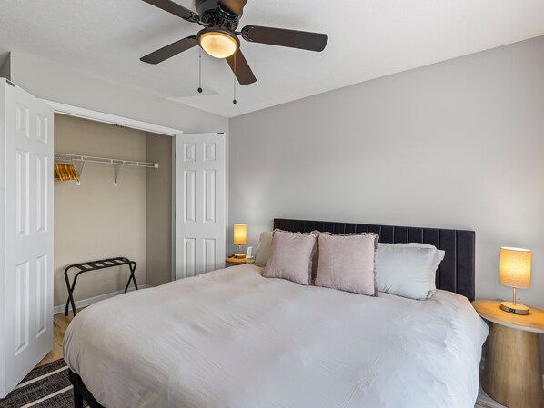A bedroom with a large bed, a ceiling fan, bedside lamps, and a wardrobe.
