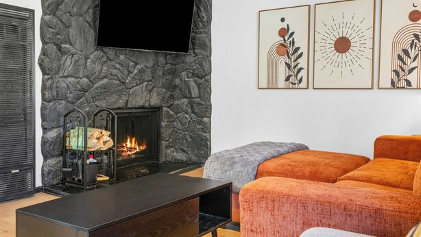 A modern living room with a stone wall, a fireplace, a flat-screen TV, and orange and gray upholstered seating. - Luxury Studio Escape - Trails & Views (Sugarloaf)