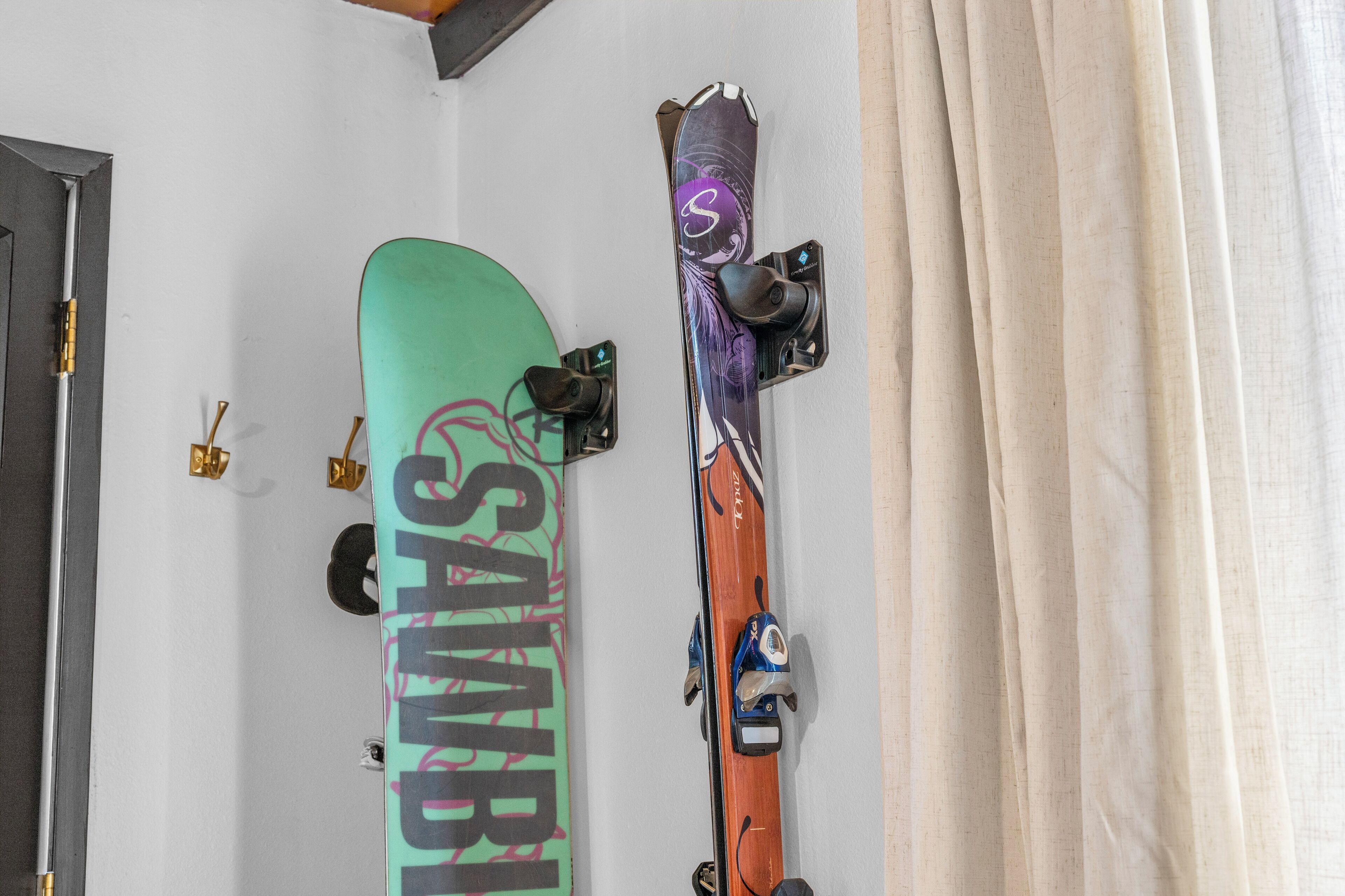 A wall with two skis and a snowboard, a door, and a curtain.