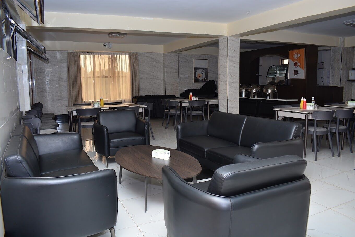 A modern hotel lobby with leather seating, a coffee machine, and a kitchen area in the background.