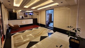 Zona de recepción de hotel con diseño moderno, que incluye un mostrador de recepción, un área de espera con alfombra roja y un suelo de gran tamaño con estampado de mármol.