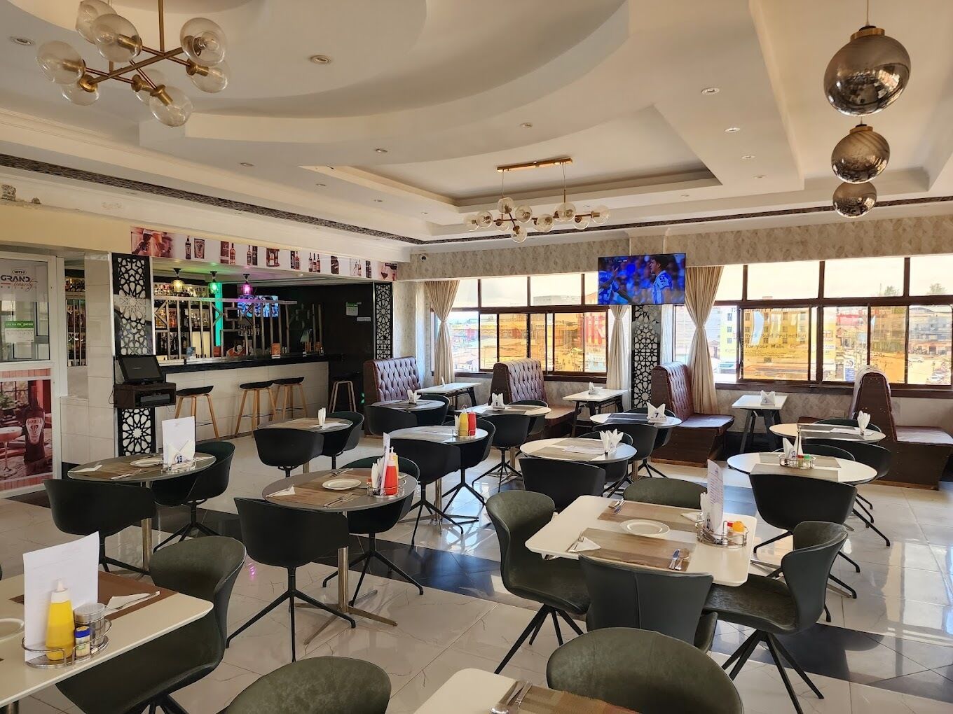 Un restaurant avec des tables et des chaises rondes, un coin bar et de grandes fenêtres.