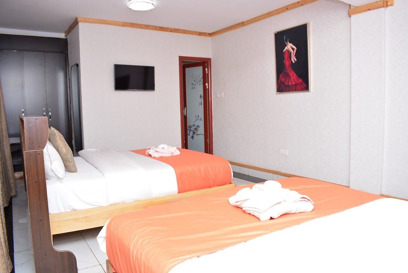 A hotel room with two beds, a wooden headboard, a flat-screen TV, and a painting on the wall.