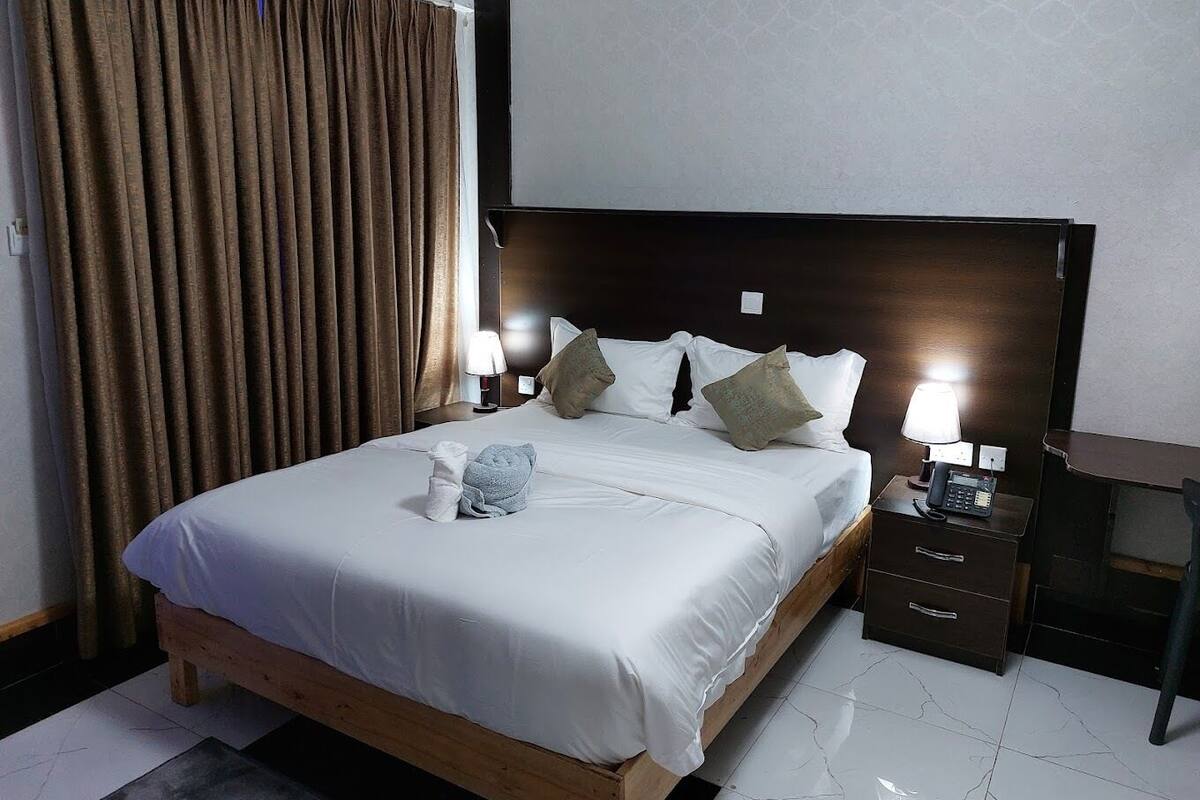 Una camera d'albergo con un letto grande, una testiera in legno, una scrivania con il telefono e un comodino con una lampada.