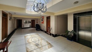 Un vestíbulo de hotel con una lámpara de araña moderna, un mostrador de recepción, un baño y un ascensor.