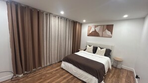 A modern bedroom with a large bed, wooden flooring, a nightstand, and a wall-mounted artwork. - Luxury sweet home (Longueuil)