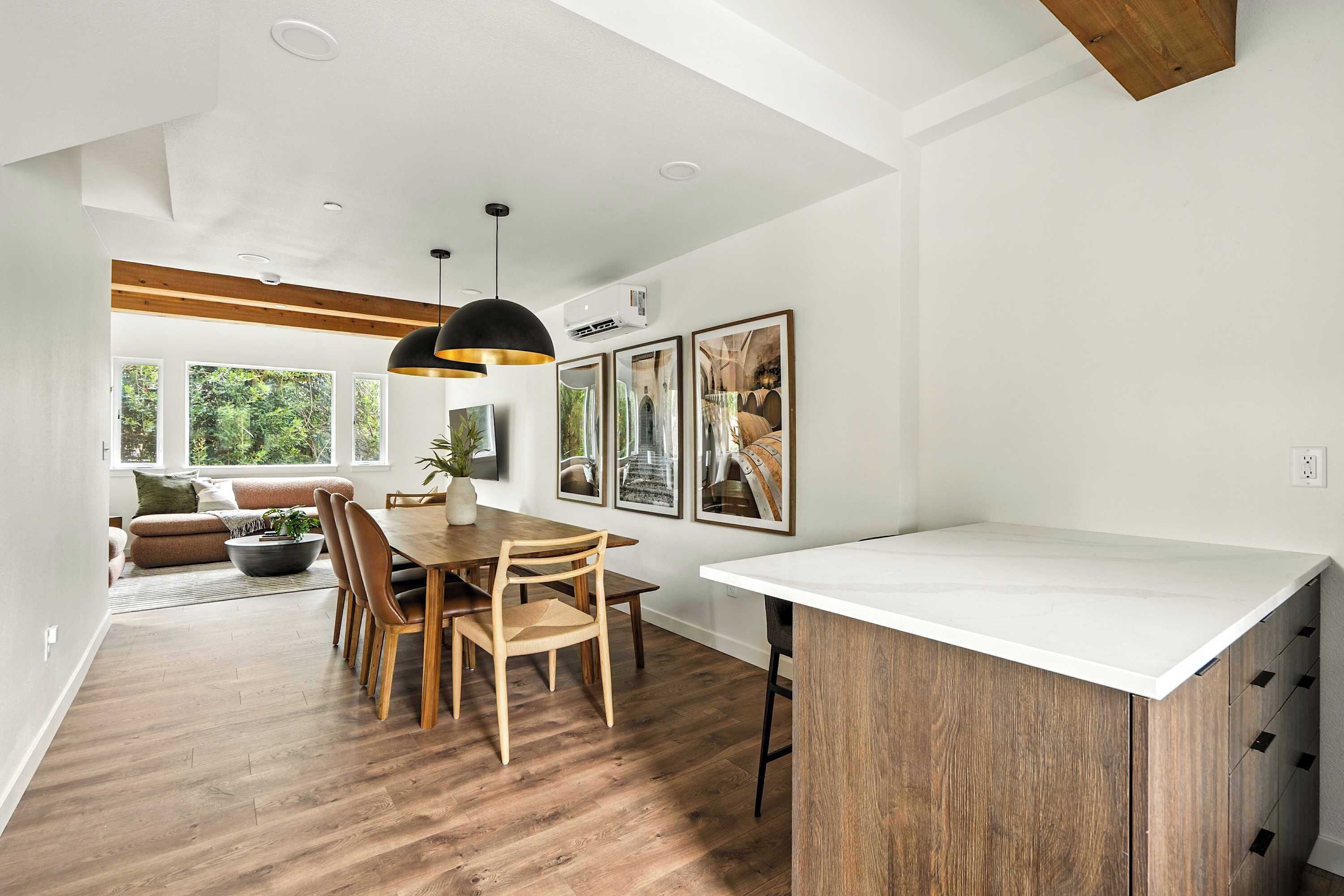 A modern kitchen with a wooden dining table, pendant lights, and a white countertop.