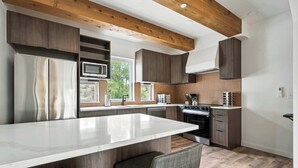 A modern kitchen with a central island, dark wood cabinetry, stainless steel appliances, and a view of the outdoors. - The Adelynn 5BR - Sleek - Spacious - Walkable (Portland)