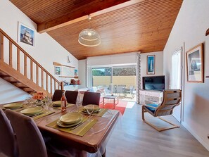 A dining area with a wooden table set for four, a TV, and a staircase leading to an upper level.