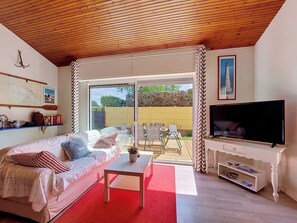 A living room with a sofa, coffee table, TV, and a sliding glass door leading to an outdoor patio.