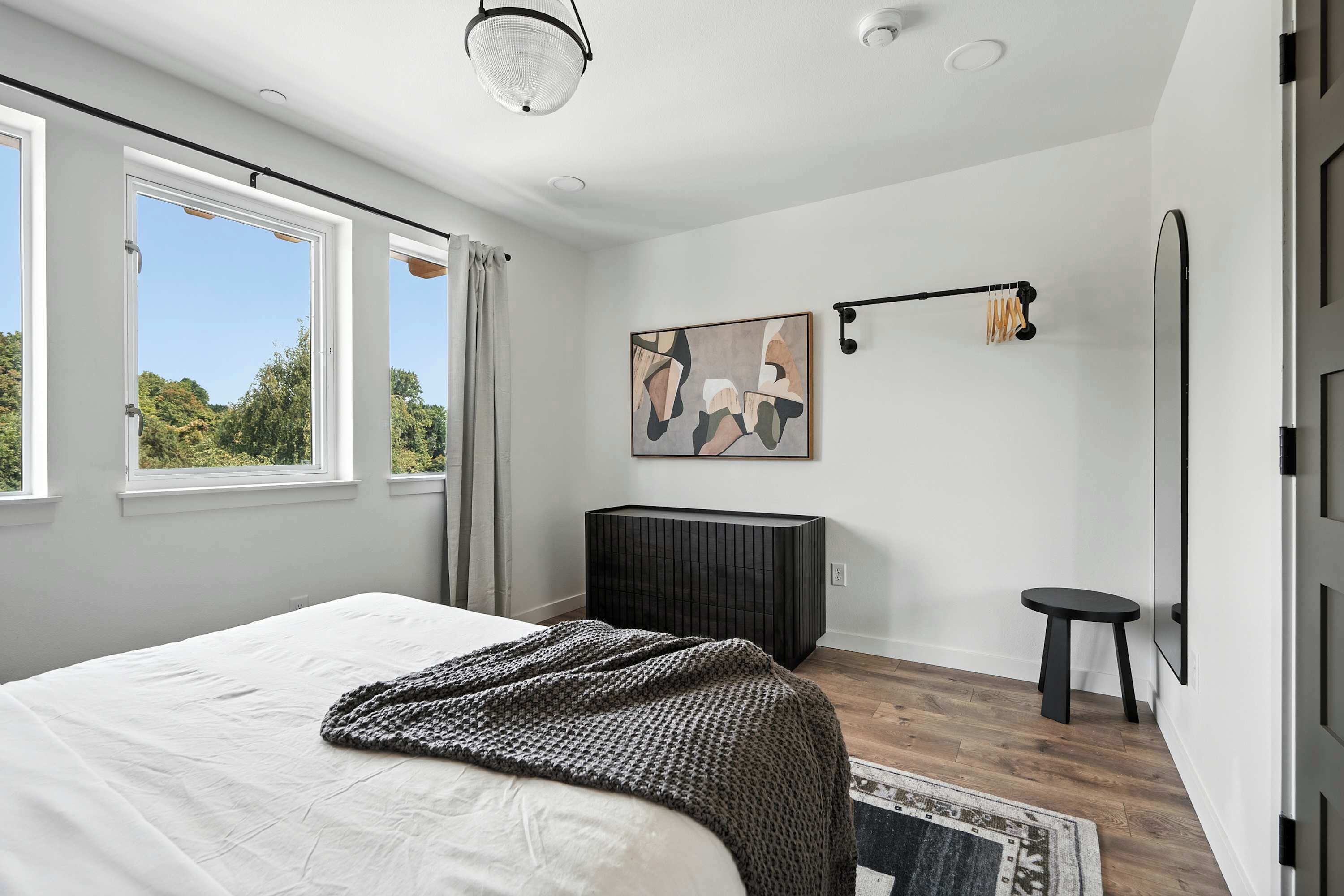 Un dormitorio moderno con una cama grande, un mueble negro, un taburete pequeño y un cuadro en la pared.