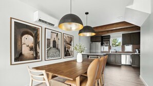 Une cuisine moderne avec une table à manger en bois, des luminaires suspendus et des tableaux encadrés accrochés au mur.