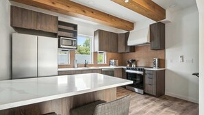 A modern kitchen with a central island, built-in appliances, and wooden beams. - New Spanish-Style Townhome in Kerns | Walk to Bars & Cafes (Portland)