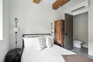 Een slaapkamer met een bed, nachtkastjes, een houten garderobe, een toilet en een airconditioning.