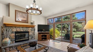 A spacious living room with a stone fireplace, a television, and a large sliding glass door leading to an outdoor patio.