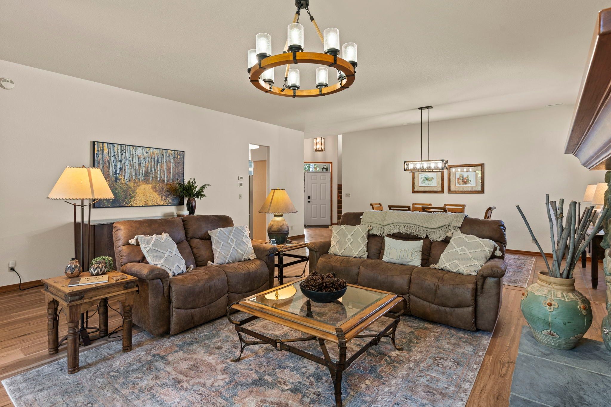 A living room with a brown leather sofa, a glass coffee table, and a chandelier.